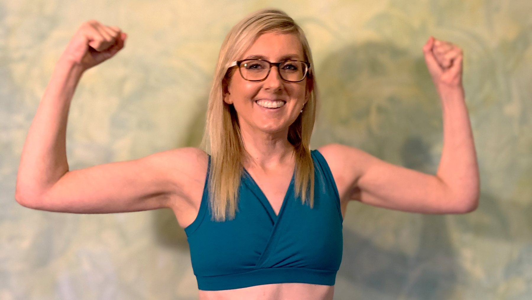 Fiona wearing a Teal Molke bra and making a strength pose with both her arms as she smiles at the camera.