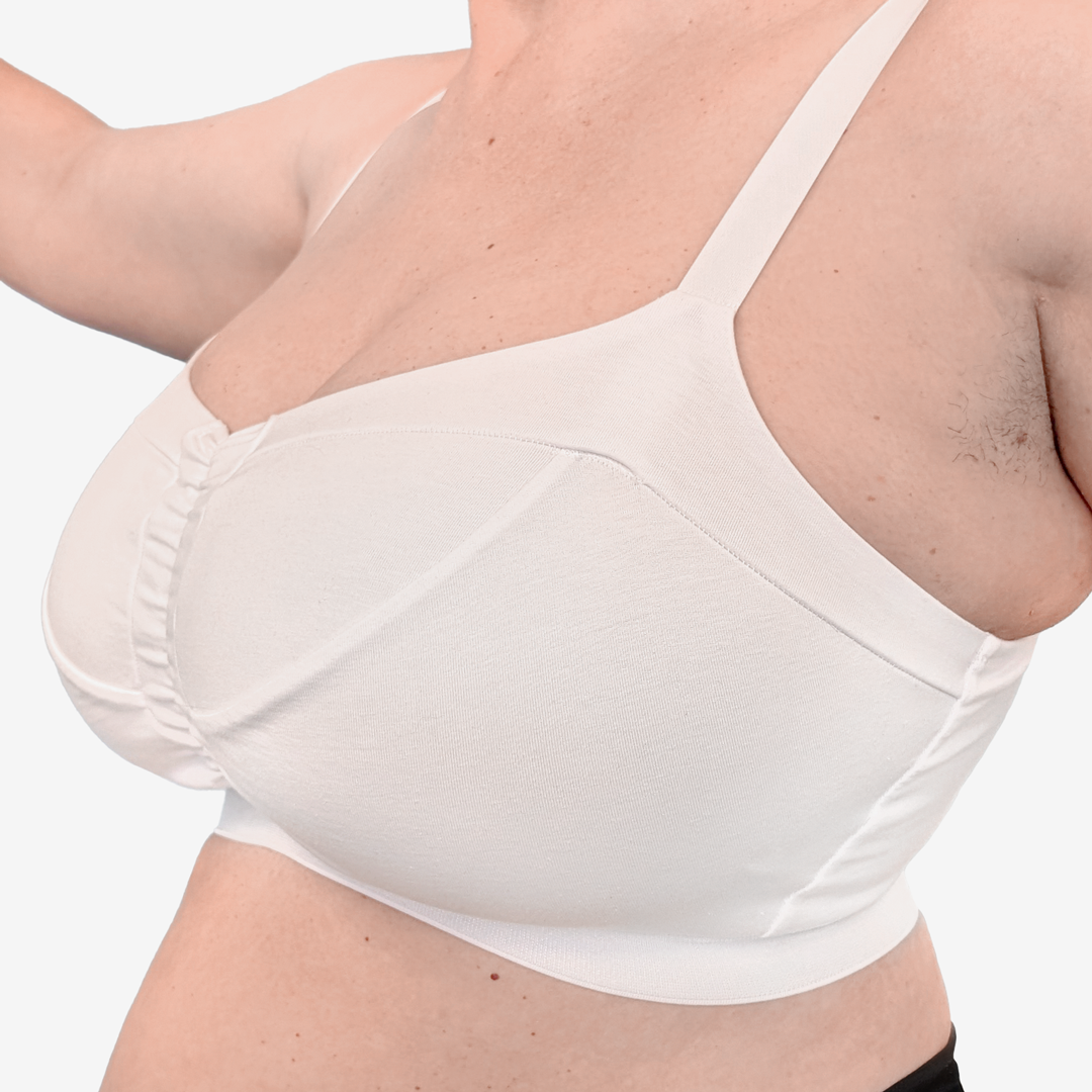 Close-up of a woman wearing a white wireless underwire bra with ruched cups and thin shoulder straps against a light gray background.