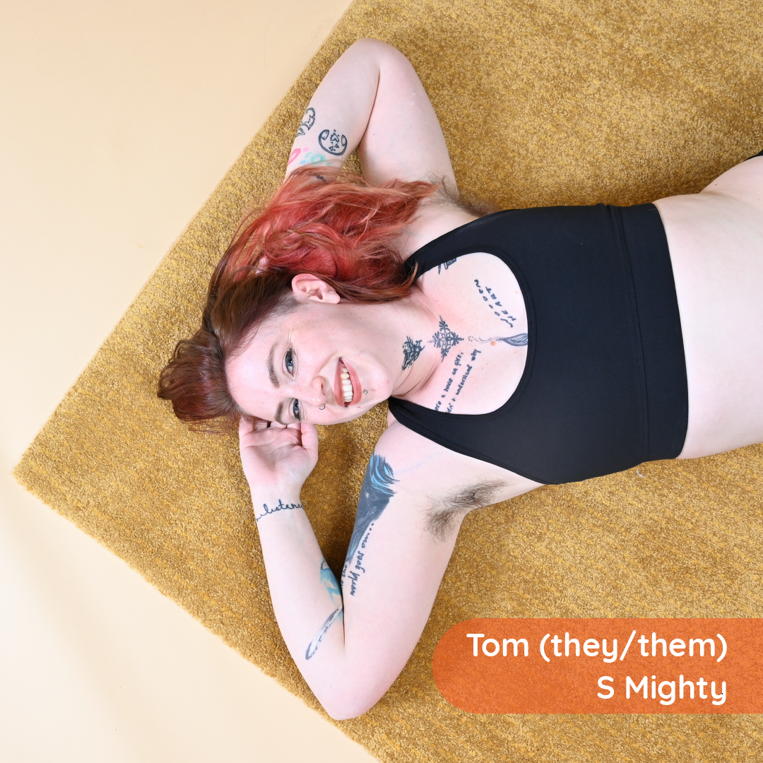 Tom is laid on a mustard rug wearing a black racerback bralette