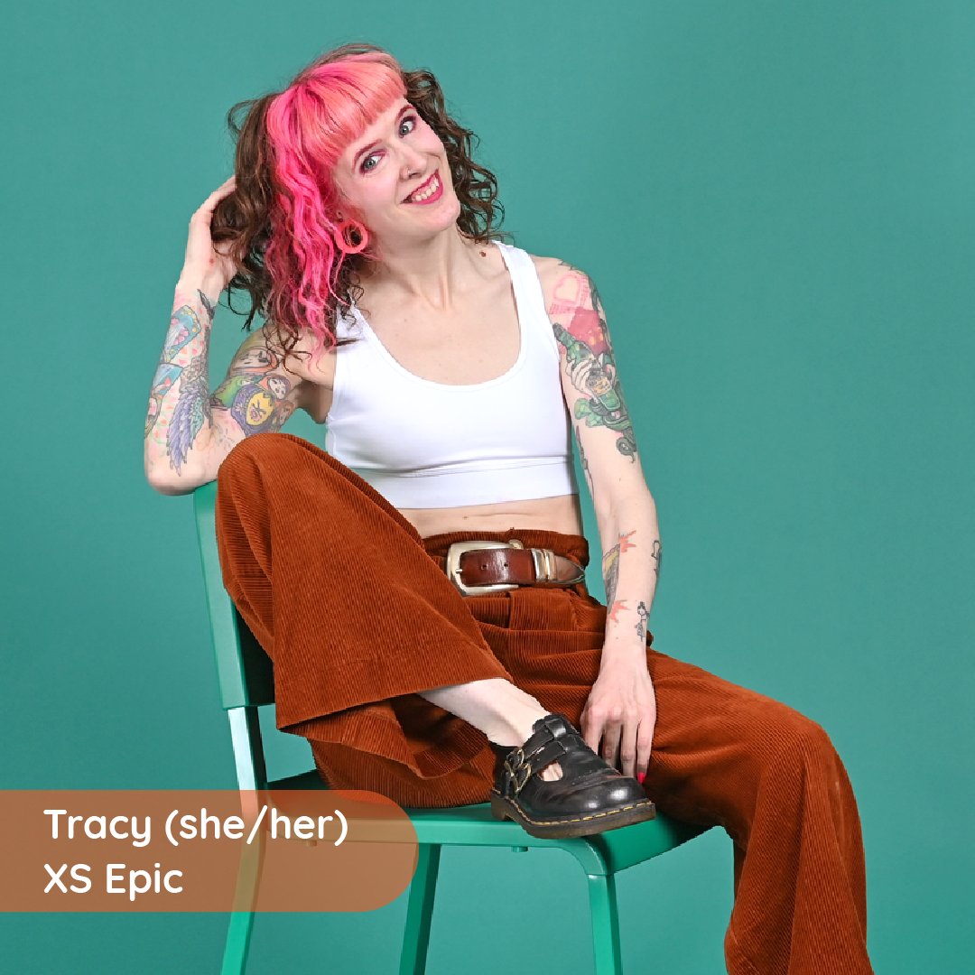 Tracy is sitting on a chair wearing a white racerback bralette and brown cord trousers