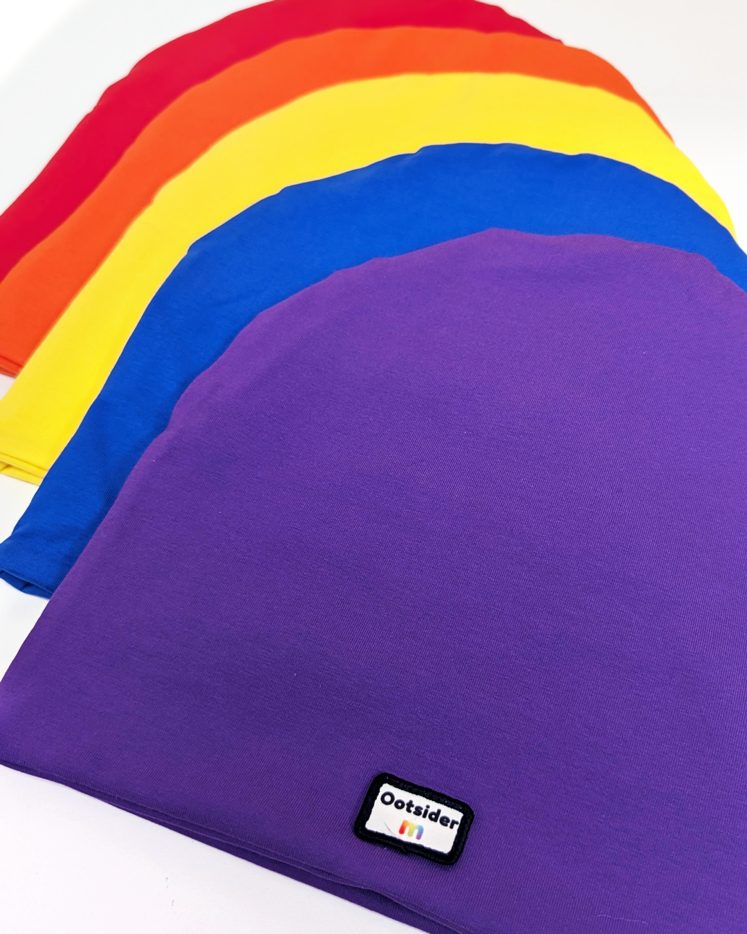 Purple beanie with 'Ootsider' label, surrounded by other coloured beanies on a white background