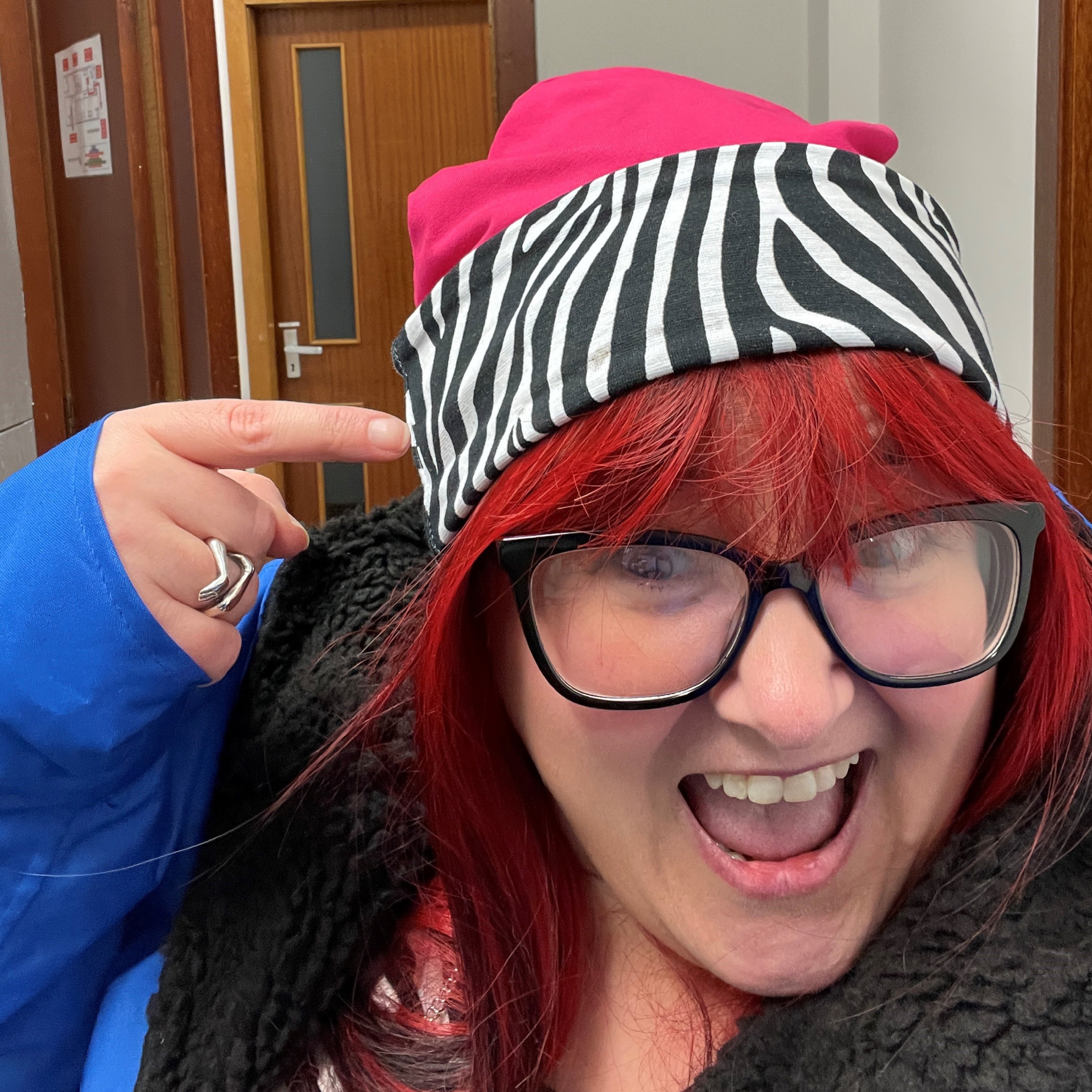 Rhona is pointing at her hat which is a Zebra and raspberry cotton beanie