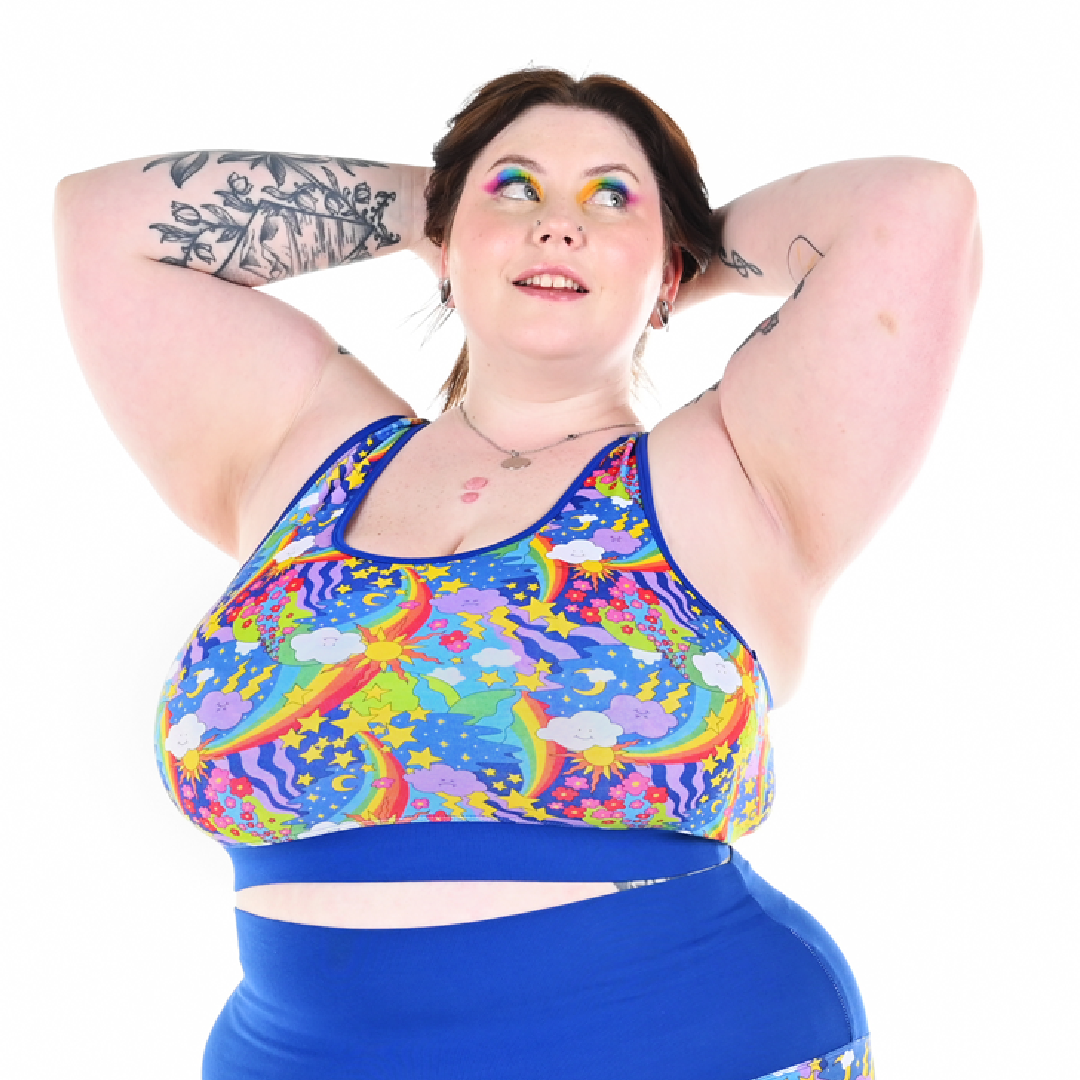 Molly has her hands behind her head wearing a retro rainbow racerback bralette