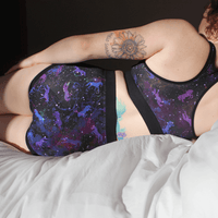 Model is wearing universe period pants and racerback bralette laid on her side on a bed