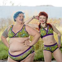 Two models wearing Dinos underwear sets. They have colourful hair and tattoos and are smiling widely.
