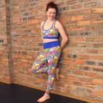 Jenni is wearing retro rainbows bright leggings and racerback bralette against an open brick wall