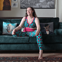 Alice is wearing teal and pink leopard print leggings and bra sitting on a sofa